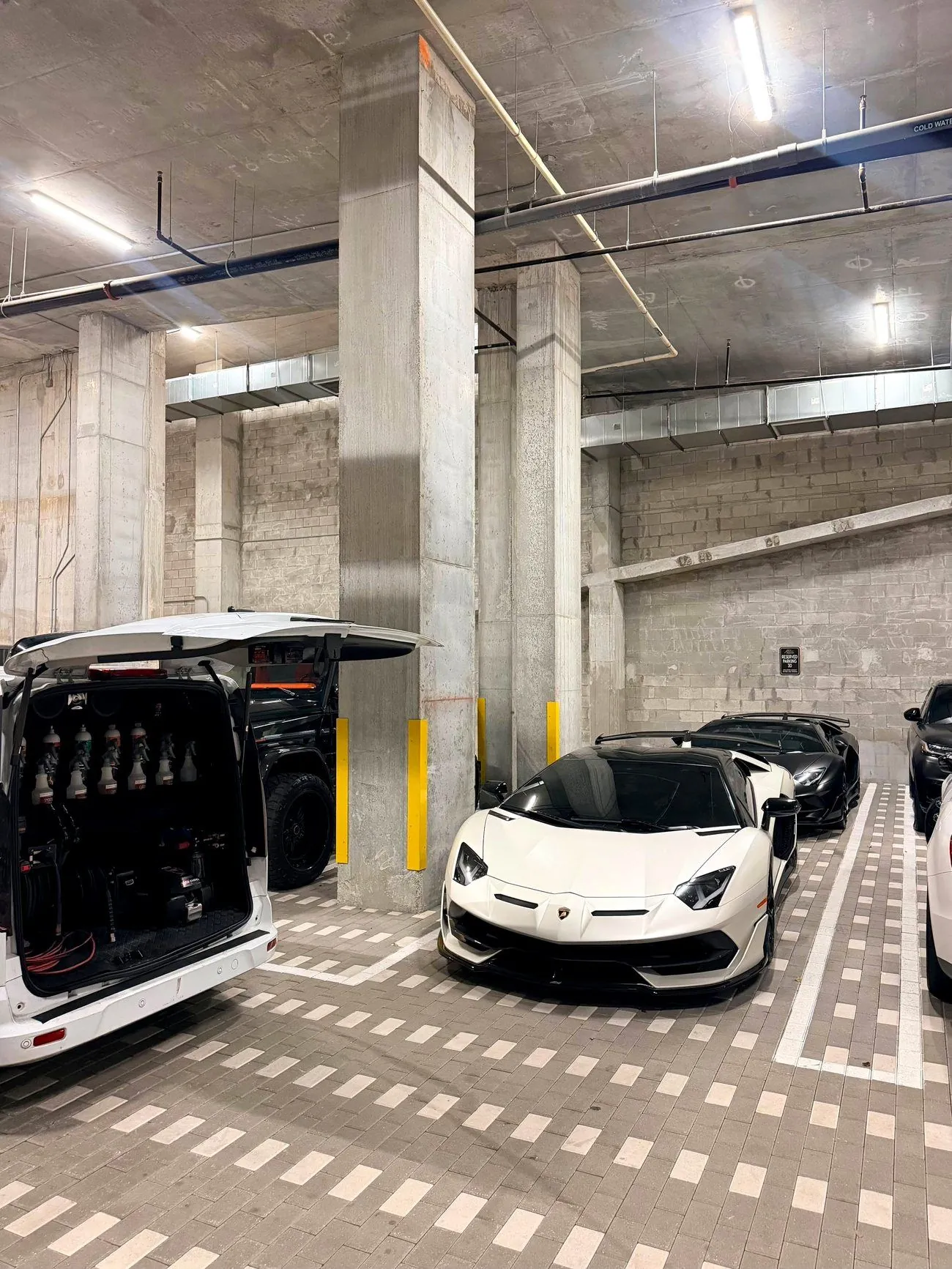 A white Lamborghini Aventador SVJ beside the Highclass van in a private garage